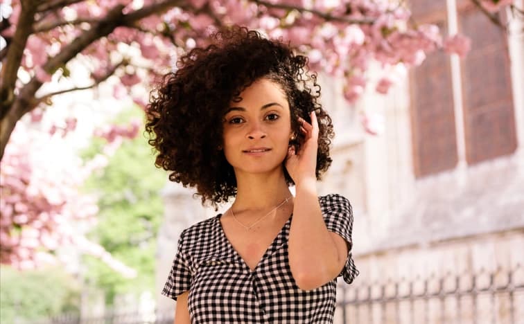 Portrait of woman with natural curly hair under cherry blossoms in Paris, spring fashion photography in gingham dress