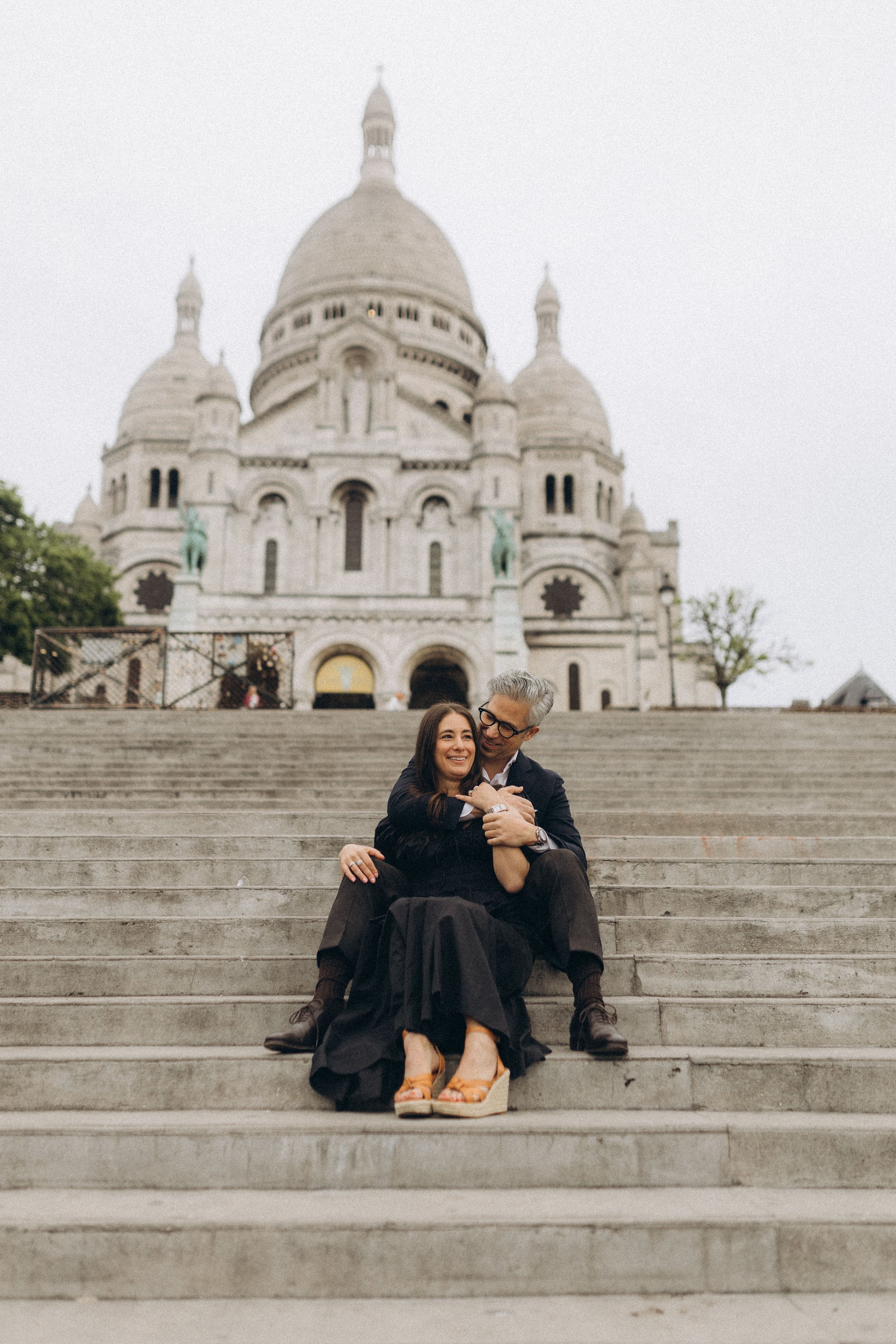 Couple sitting on the steps of the Sacré-Cœur basilica, embracing with the white domes visible in the background
