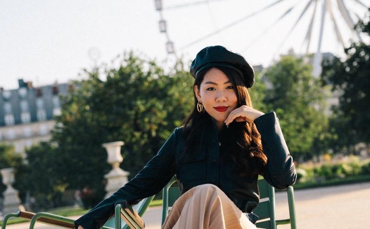 Young woman wearing a dark beret, seated in a classic green chair in the Tuileries Garden with the Ferris wheel in the background