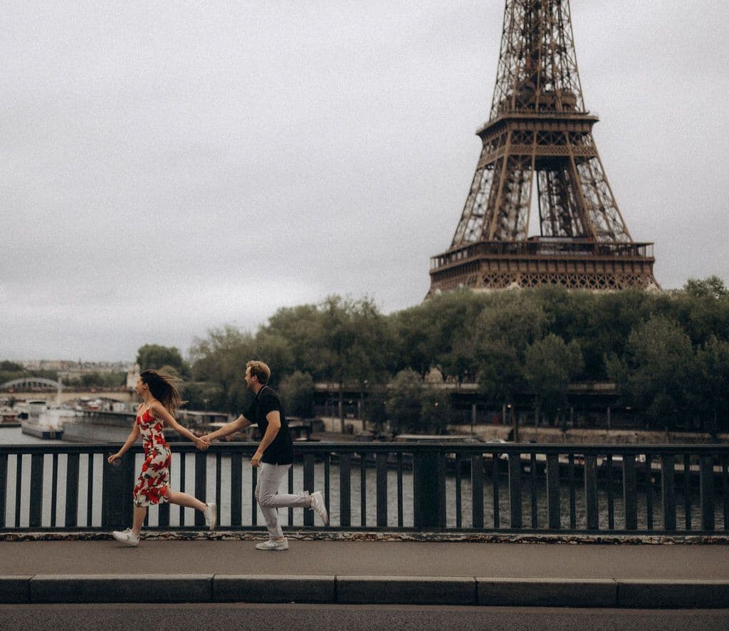 Newly engaged couple running hand in hand on the Bir-Hakeim bridge, Eiffel Tower in the background