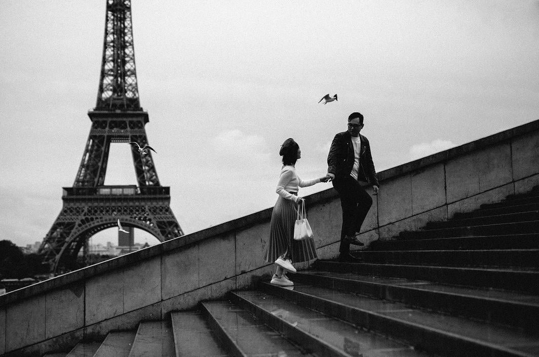 Couple walking up the Trocadéro stairs holding hands, with the Eiffel Tower behind them, in black and white